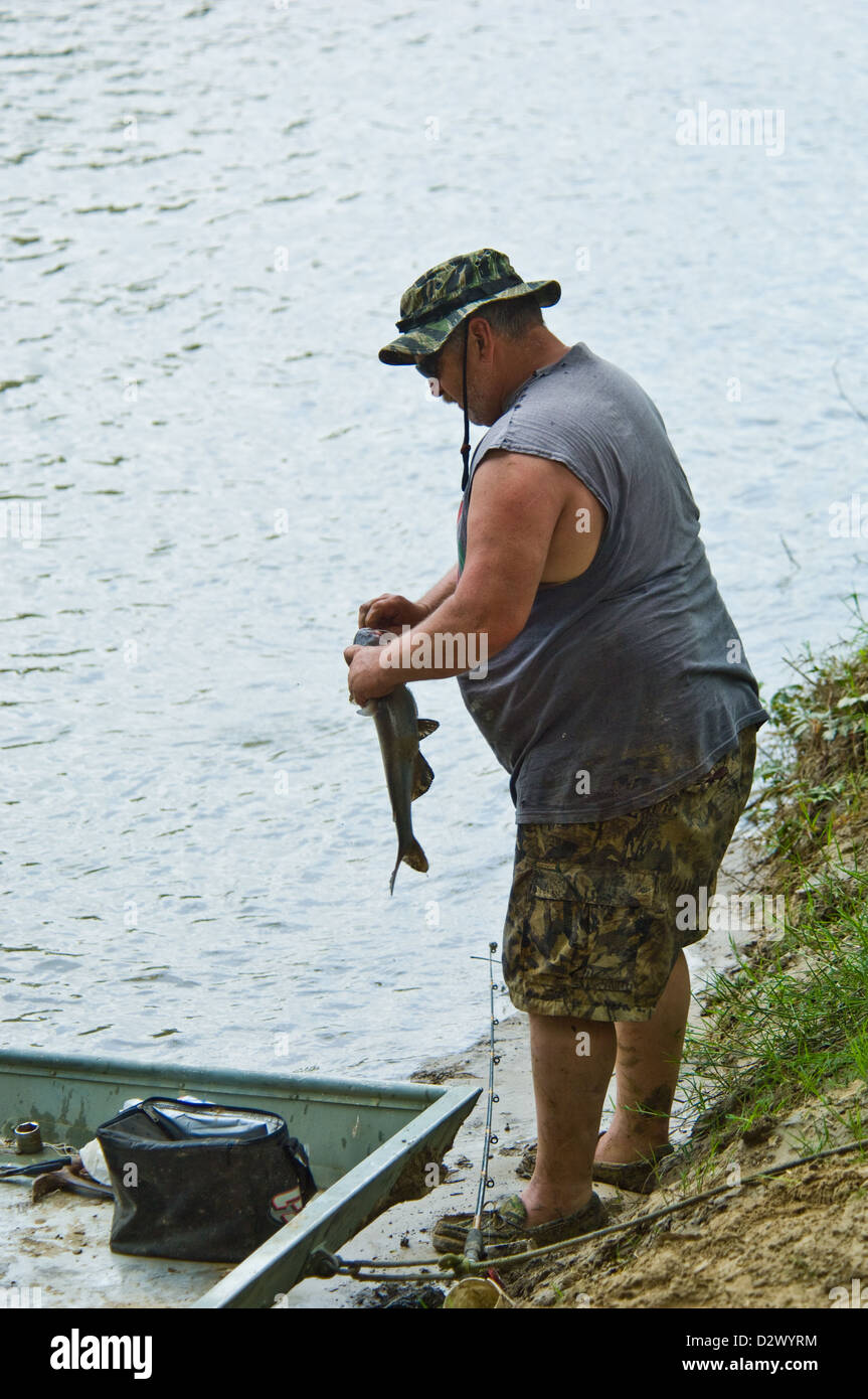 Large man unhooking a catfish on the Guadalupe River bank near Cuero