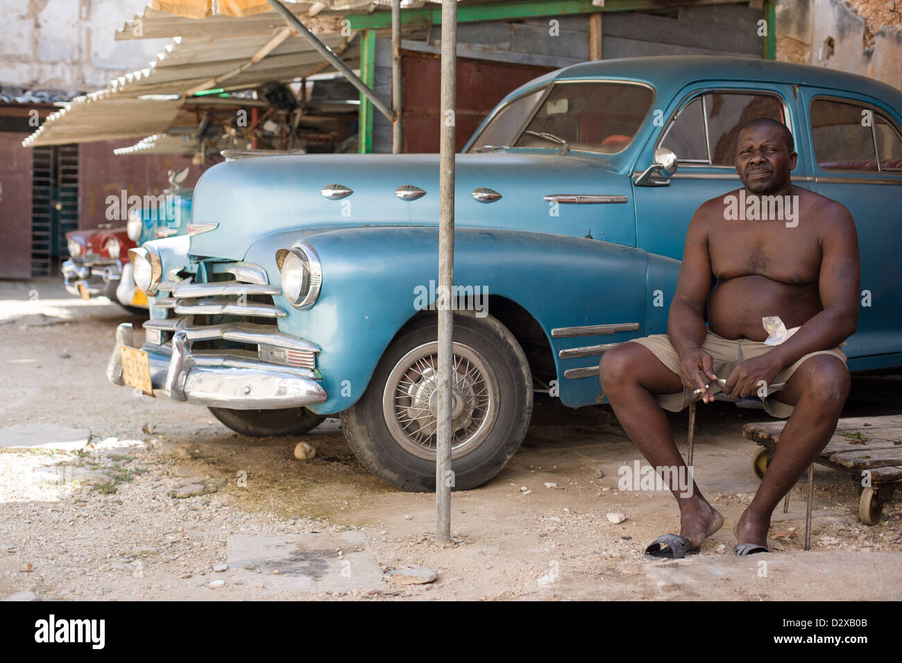 A man sitting next to an old American car in Havana, Cuba Stock Photo
