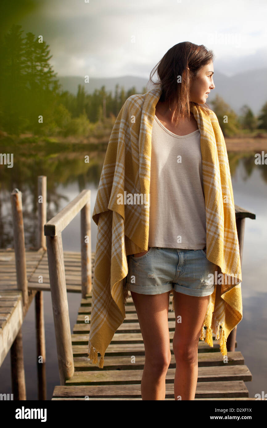 Woman wrapped in blanket standing on dock over lake Stock Photo