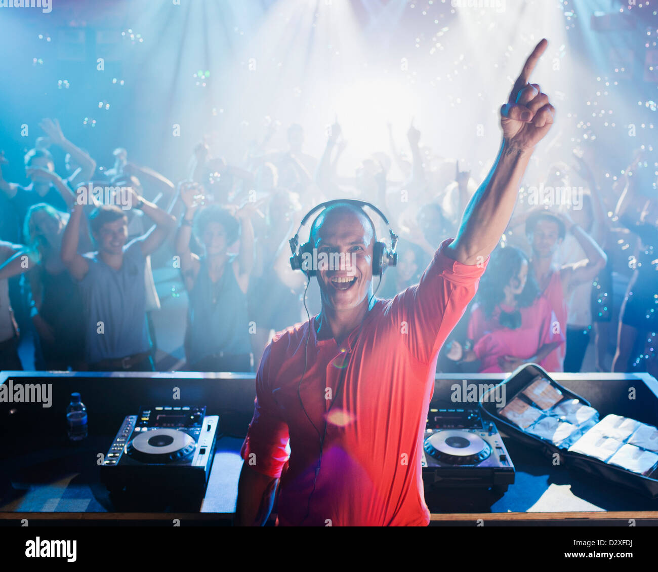 Portrait of enthusiastic DJ with arm raised and people on dance floor in background Stock Photo
