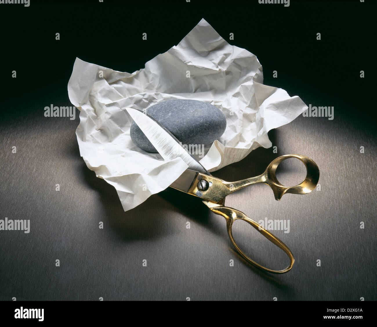 Scissors cutting into paper with rock Stock Photo