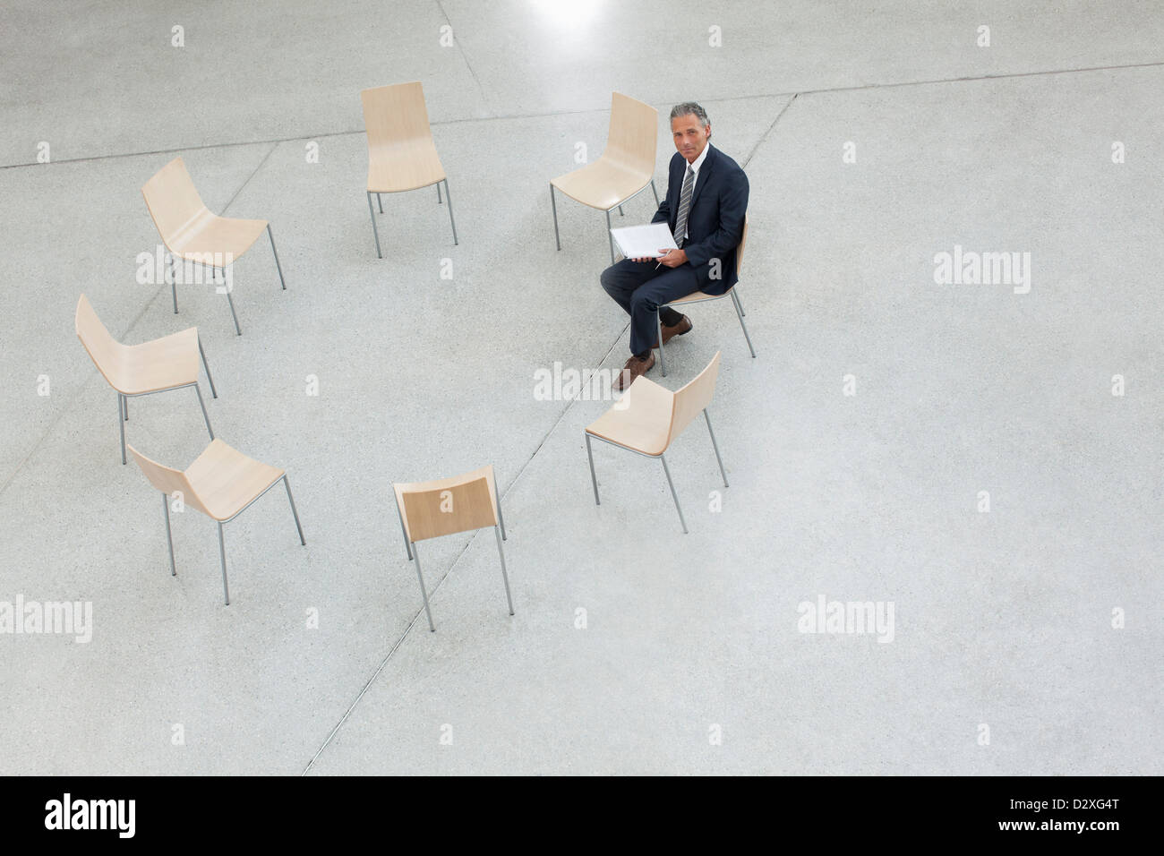 Portrait of smiling businessman sitting in circle of chairs Stock Photo