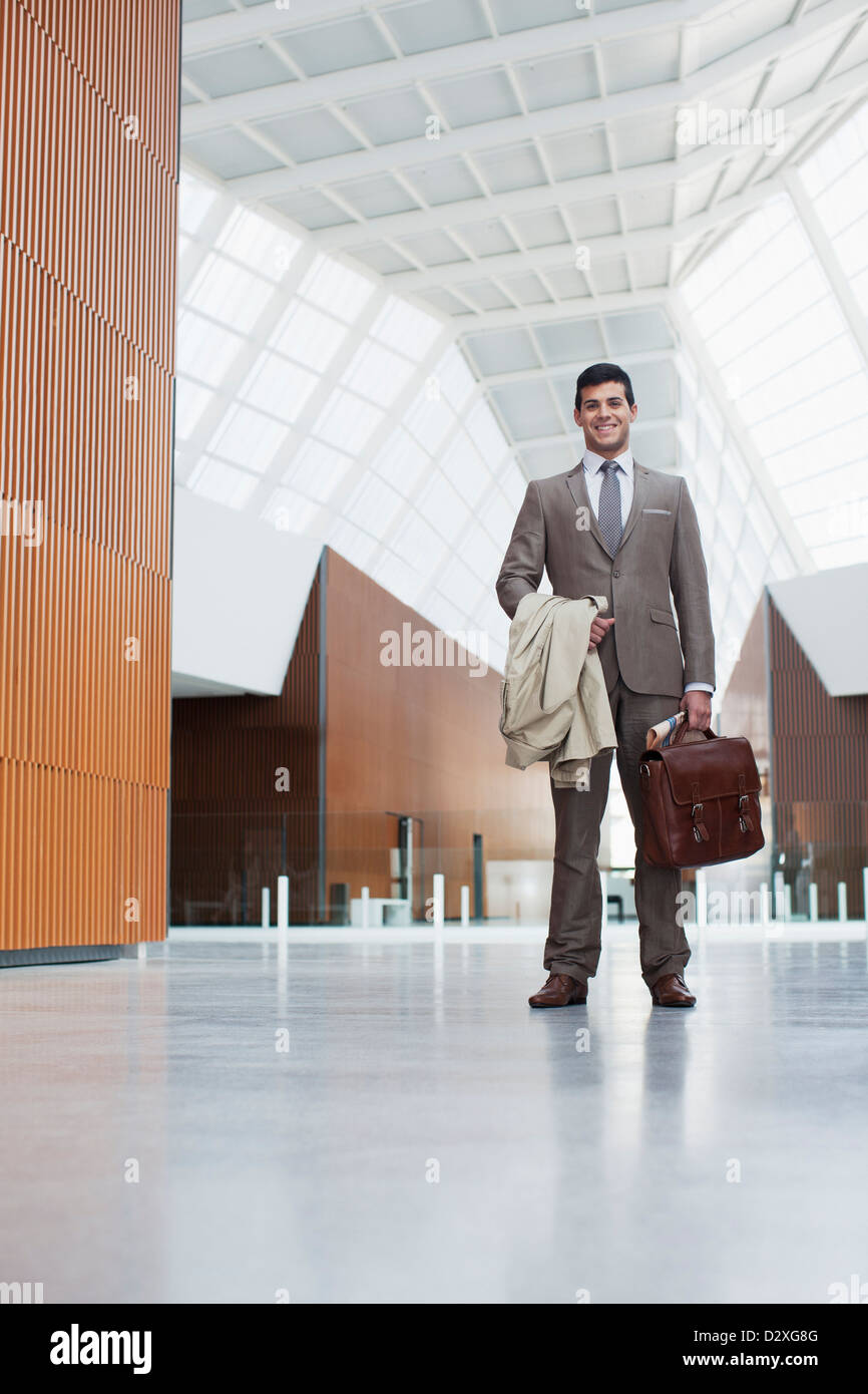 Portrait of smiling businessman holding coat and briefcase in lobby Stock Photo