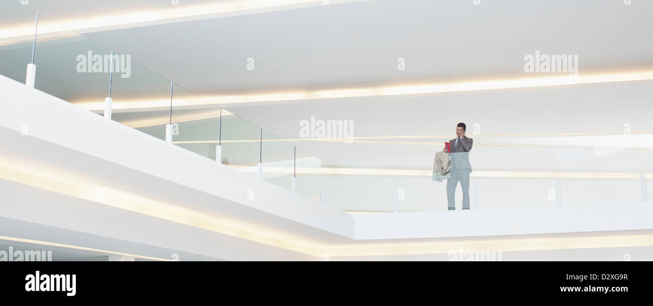 Businessman at glass balcony railing in modern office Stock Photo