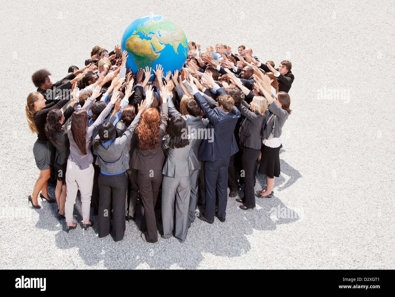 Crowd of business people in huddle reaching for globe Stock Photo