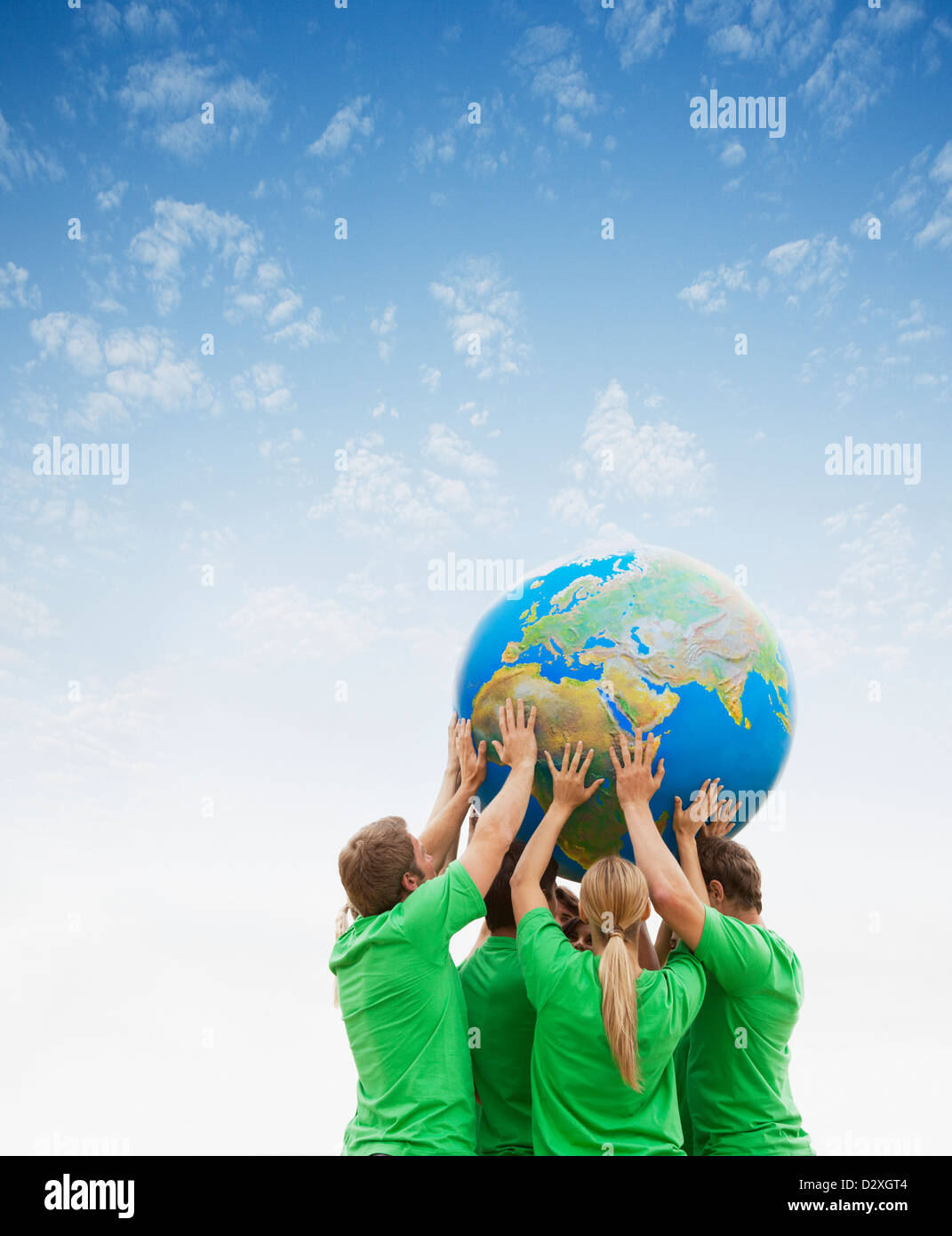 Team in green t-shirts lifting globe overhead Stock Photo