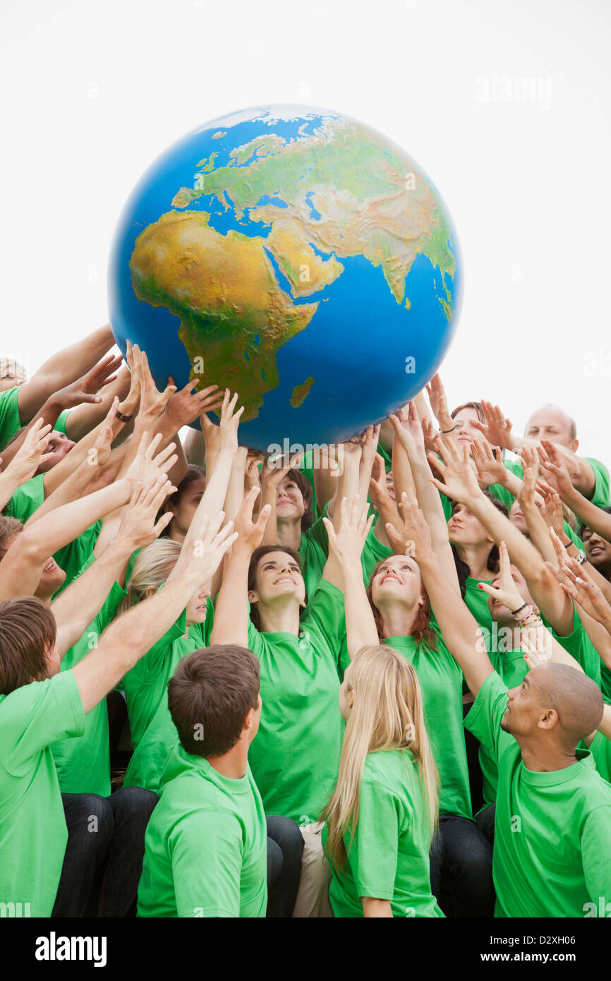 Team in green t-shirts reaching for globe overhead Stock Photo