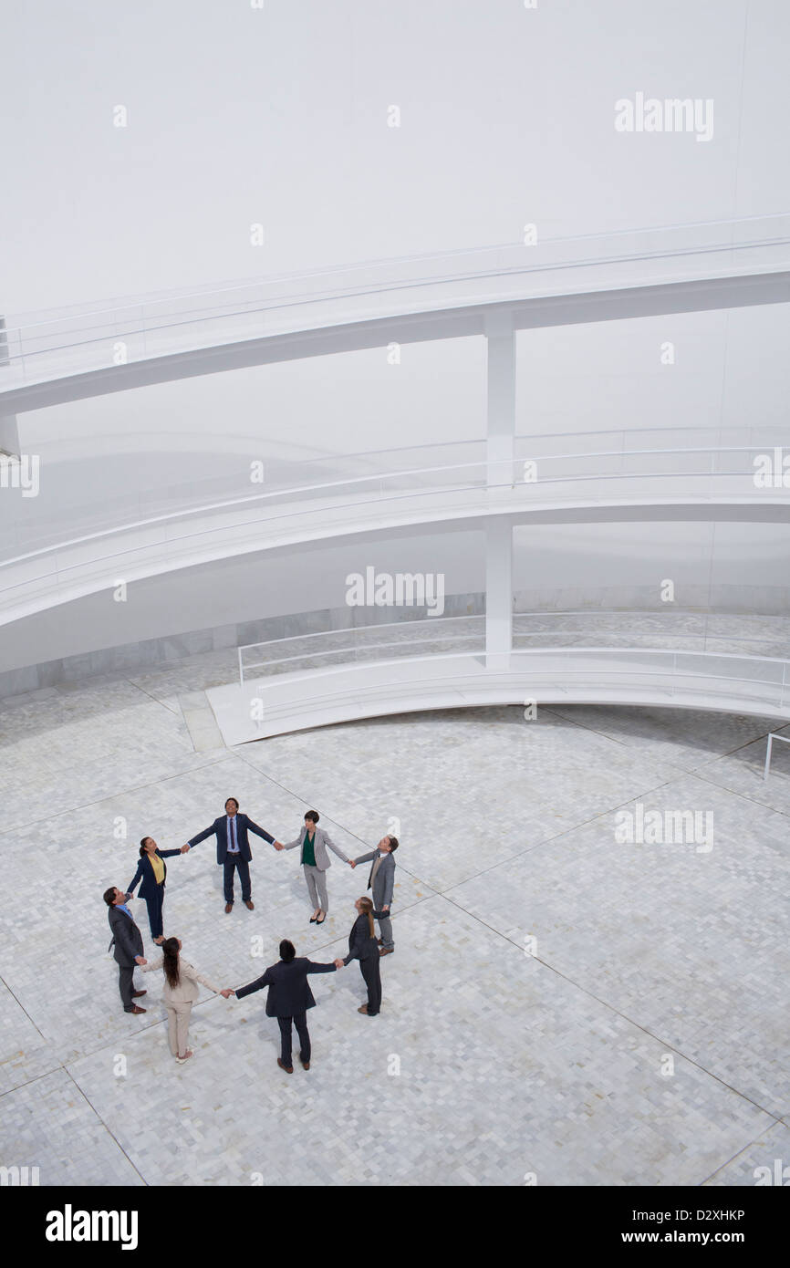 Business people holding hands and standing in circle in modern courtyard Stock Photo