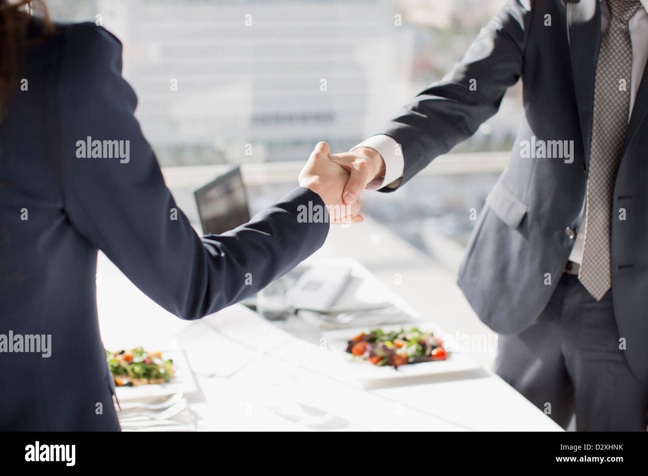 Businessman and businesswoman shaking hands at table with lunch Stock Photo