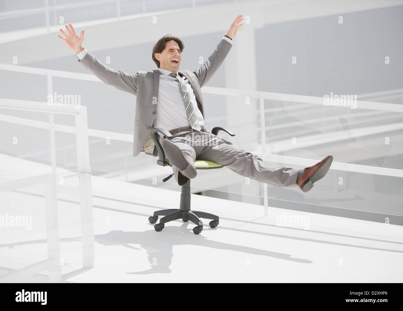 Carefree businessman sliding down walkway on office chair with wheels