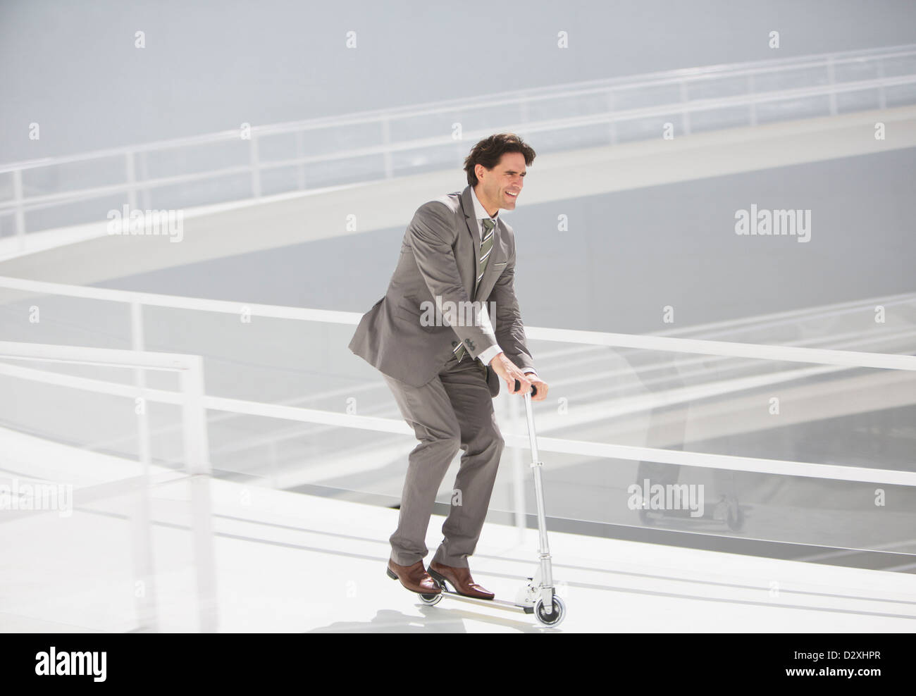 Businessman riding scooter down walkway Stock Photo