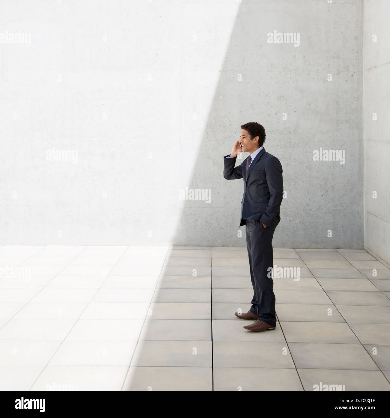Businessman standing in shade and talking on cell phone Stock Photo