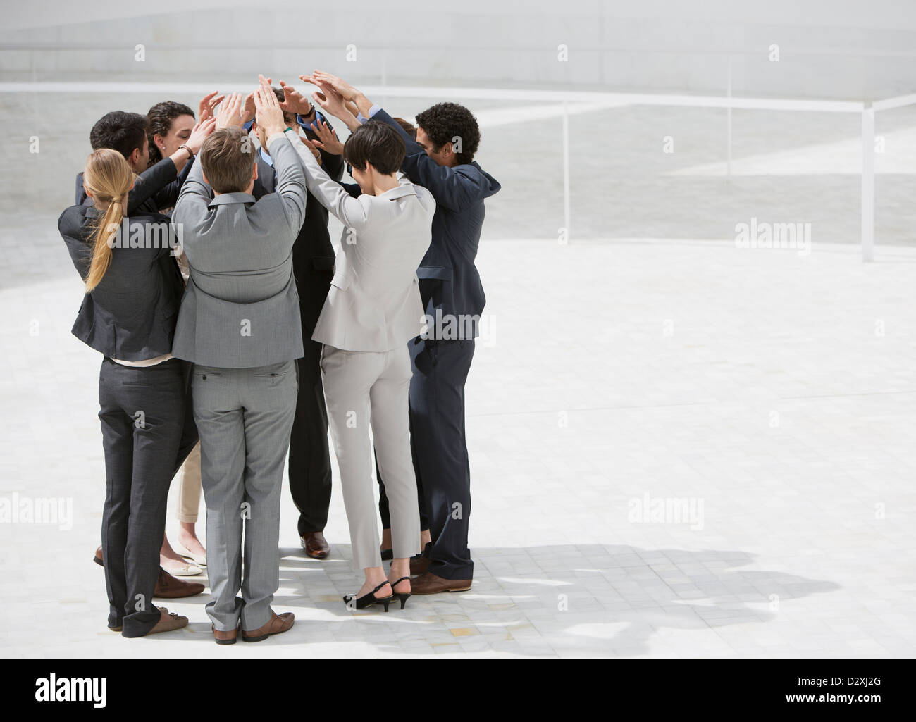 Business people standing in huddle with arms raised Stock Photo
