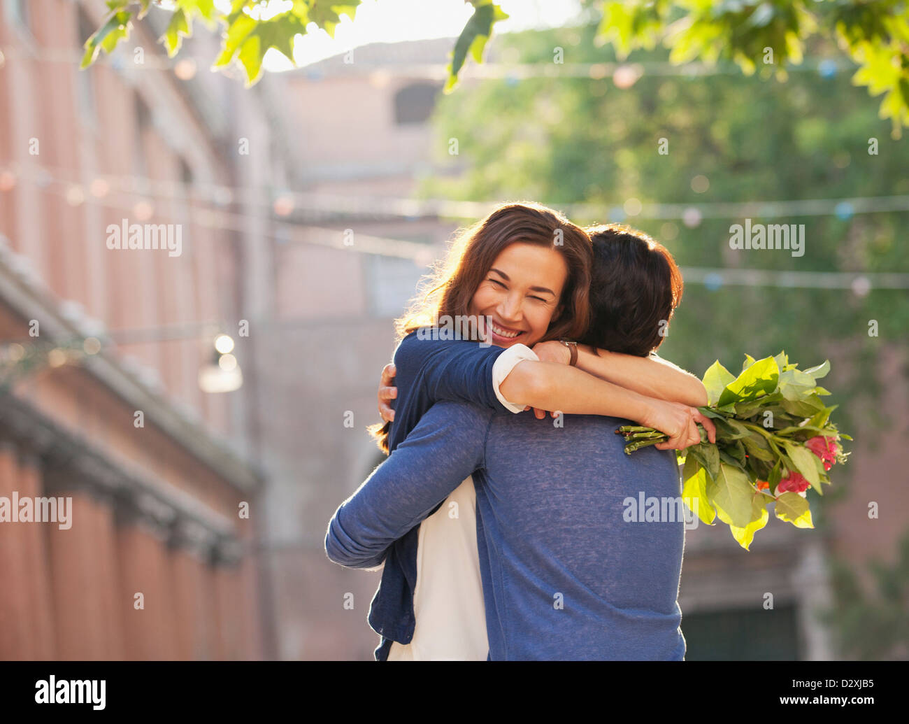 Smiling woman with flowers hugging man Stock Photo