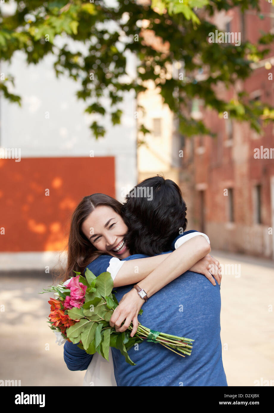 Smiling woman with flowers hugging man Stock Photo