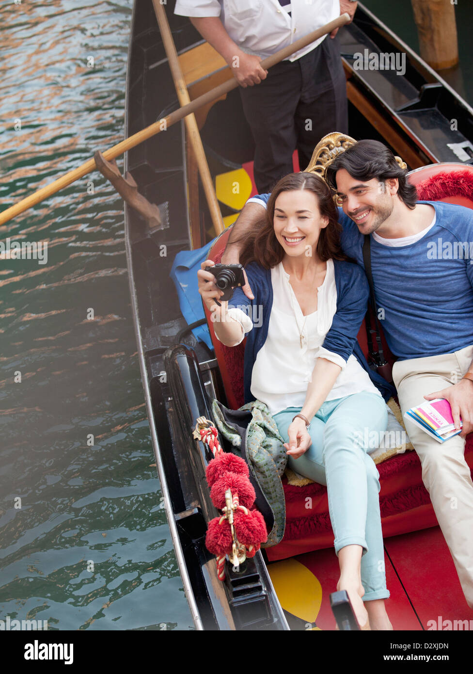 Smiling couple taking photographs in gondola on canal in Venice Stock Photo