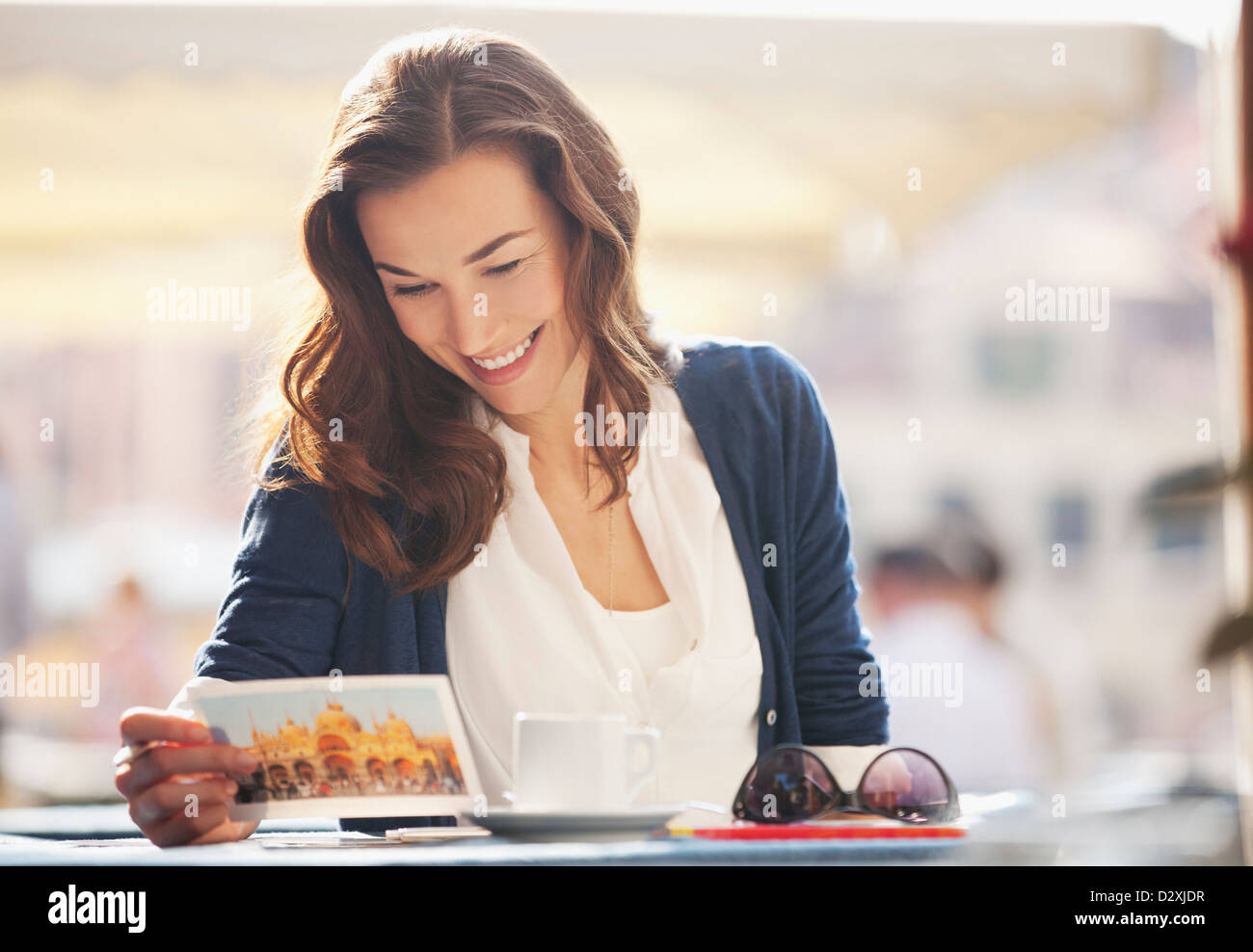 Smiling woman reading postcard at sidewalk cafe Stock Photo