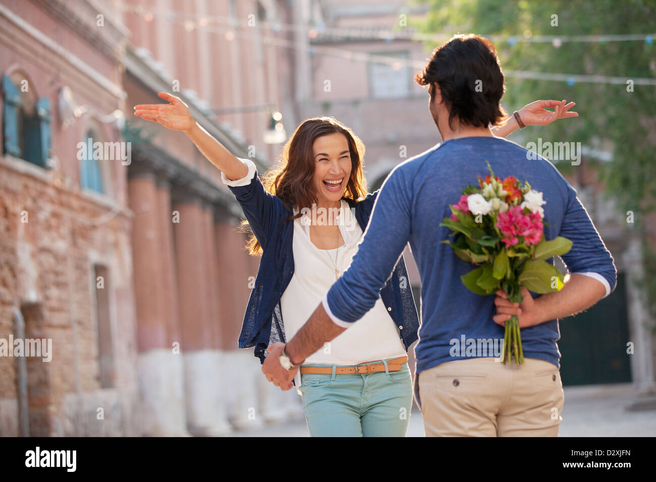 Enthusiastic woman approaching man with flowers behind back Stock Photo