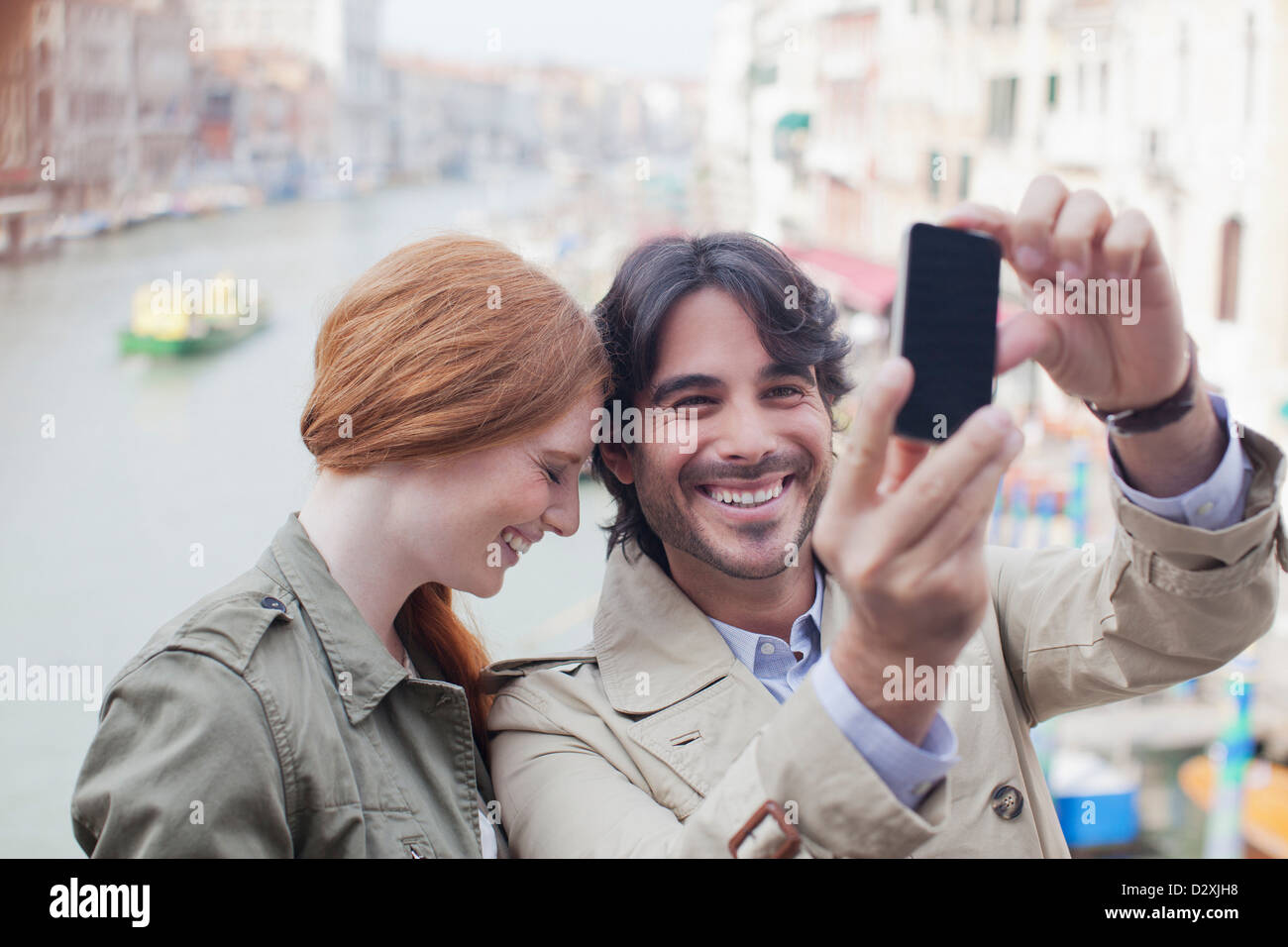 Laughing couple taking self-portrait with camera phone on canal in Venice Stock Photo