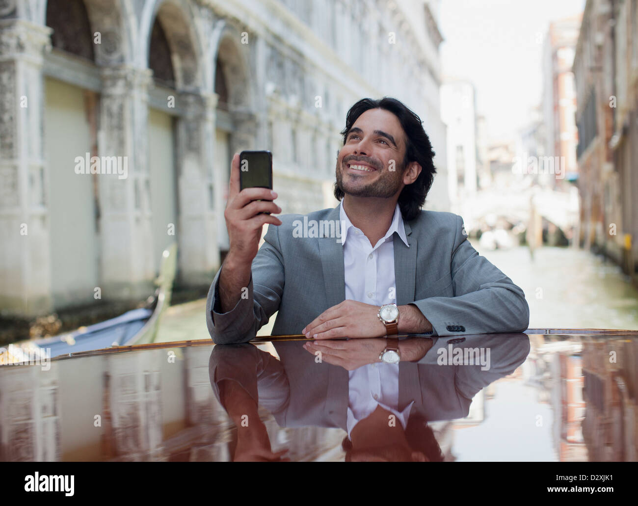 Smiling businessman holding cell phone and leaning on boat in canal in Venice Stock Photo