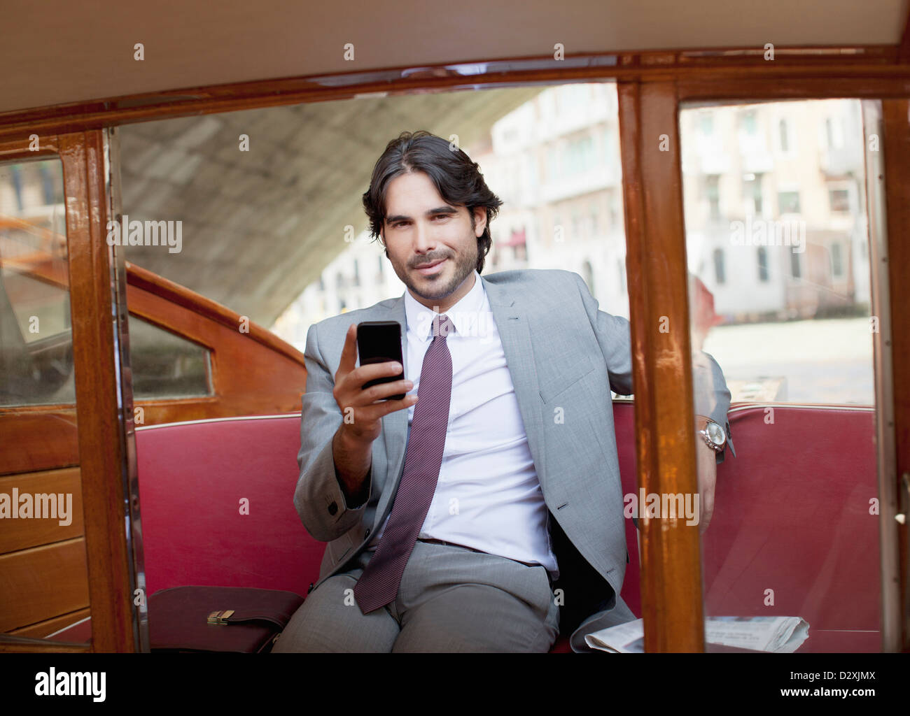 Portrait of smiling businessman with cell phone on boat in Venice Stock Photo