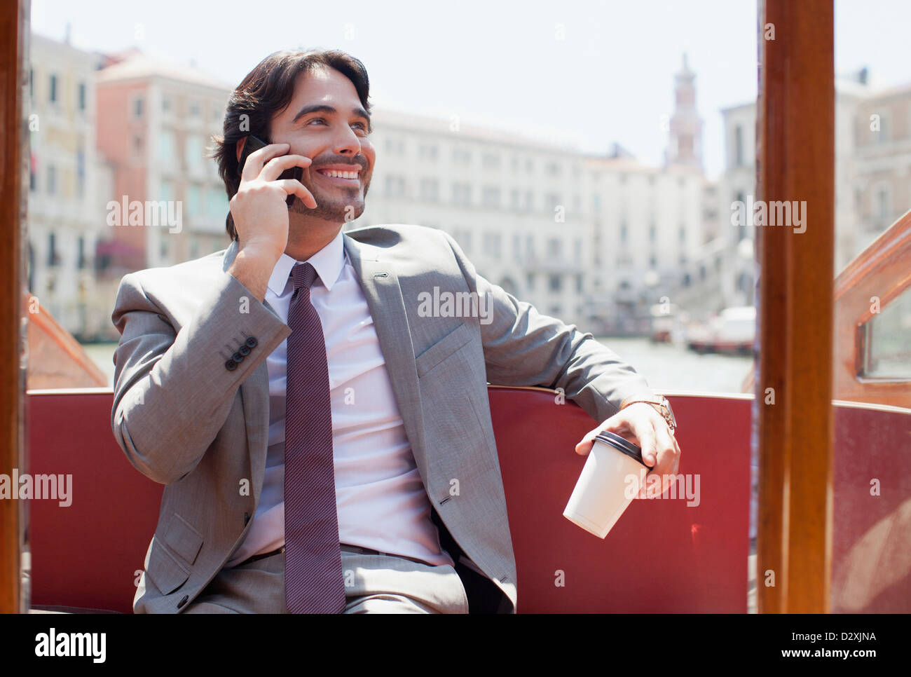 Smiling businessman with coffee talking on cell phone on boat in Venice Stock Photo