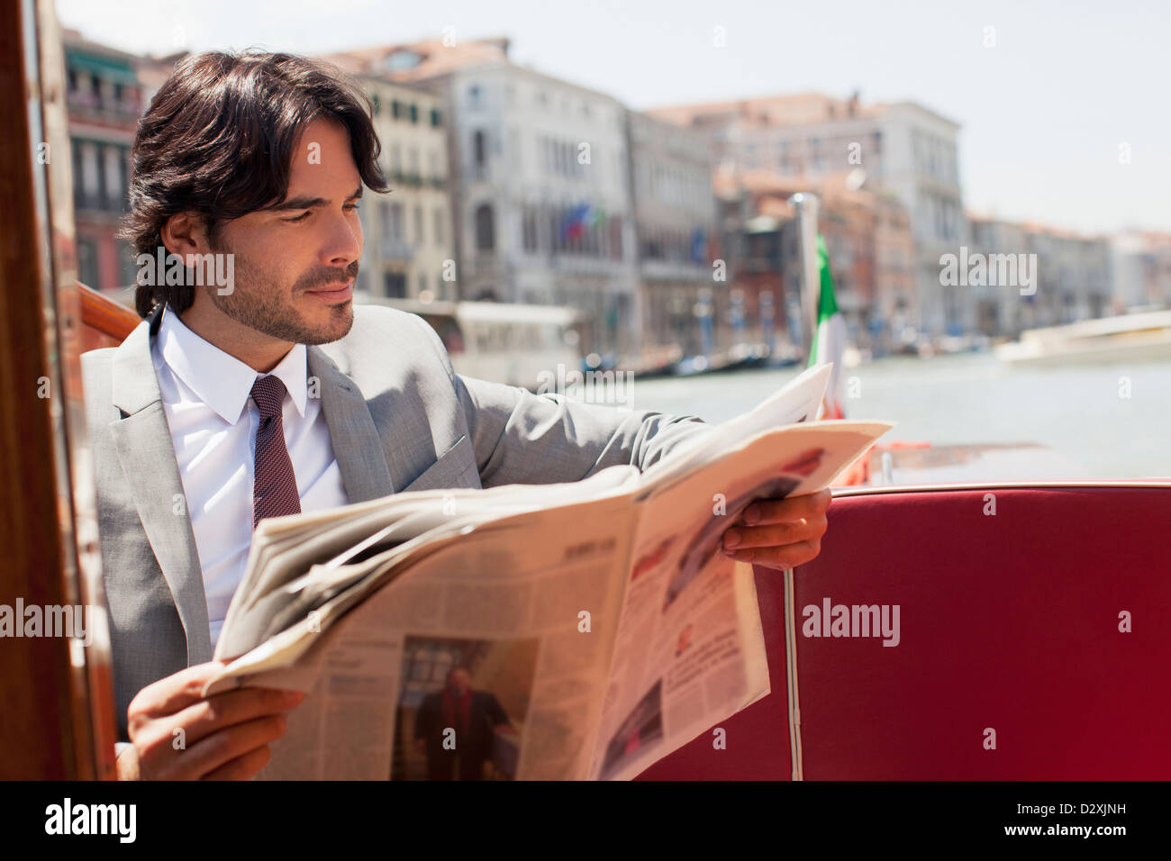 Businessman reading newspaper on boat in Venice Stock Photo