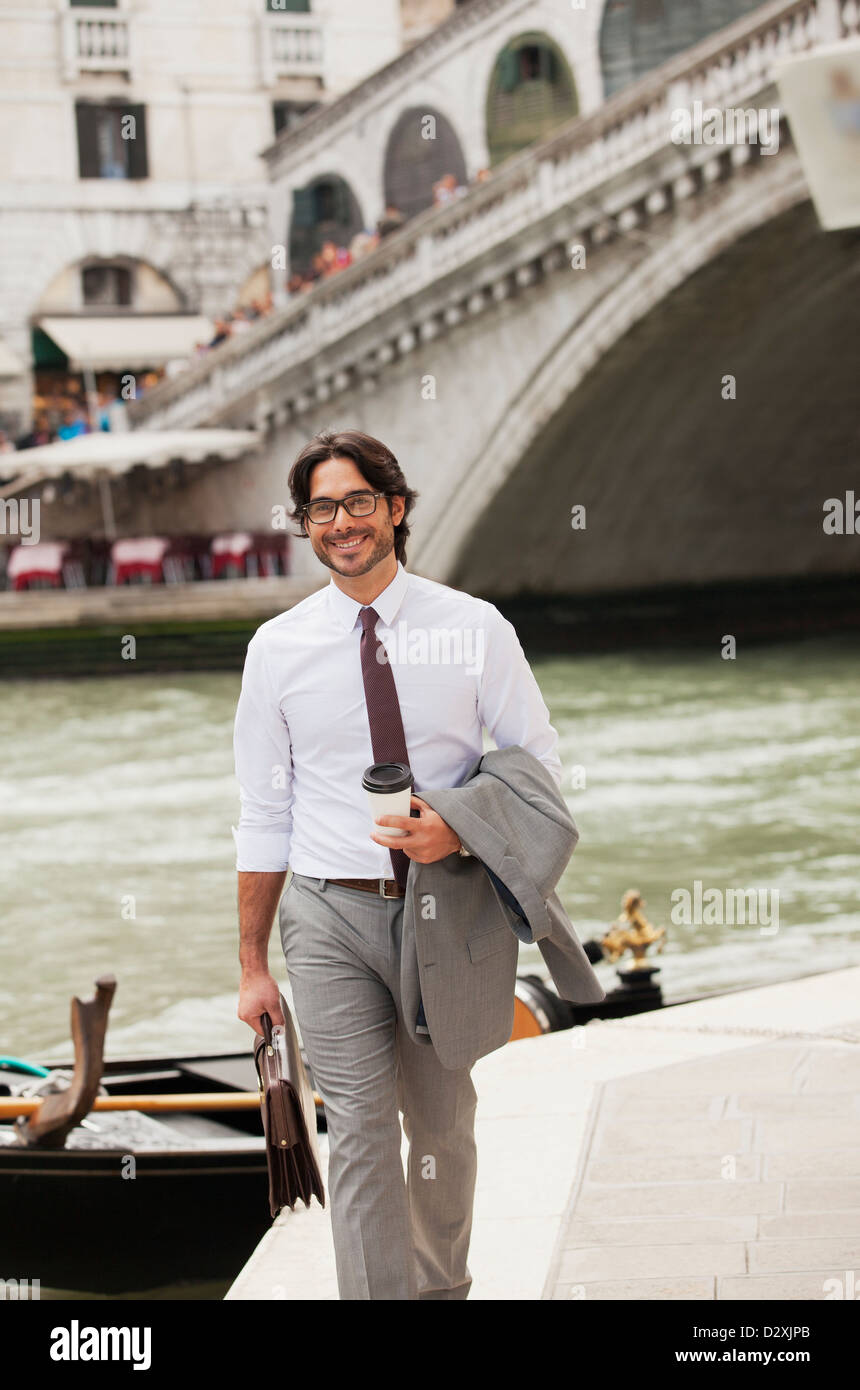 Portrait of smiling businessman with coffee walking along canal in Venice Stock Photo