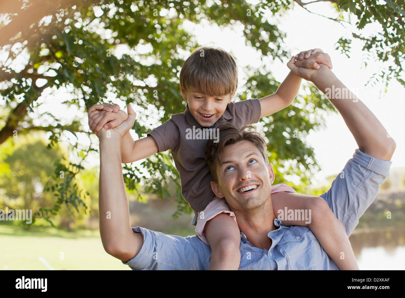 Smiling father carrying son on shoulders under tree Stock Photo