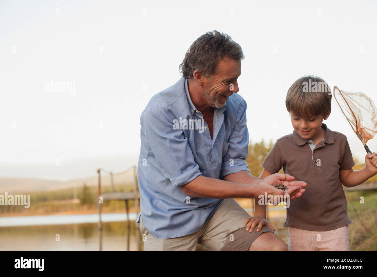 Smiling grandfather and grandson fishing at lakeside Stock Photo