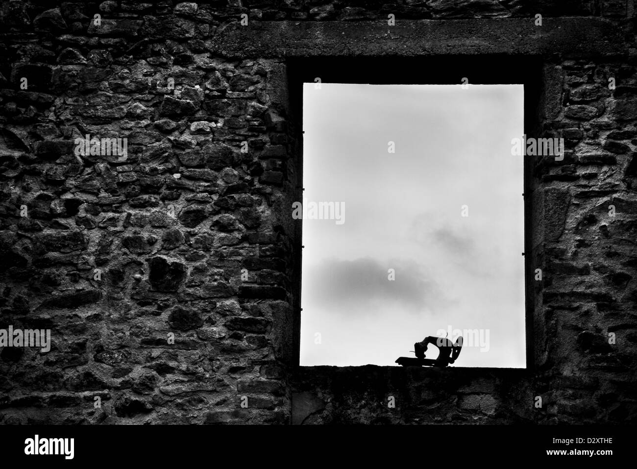 A fire damaged sewing machine silhouette in a window frame in a destroyed house. Stock Photo