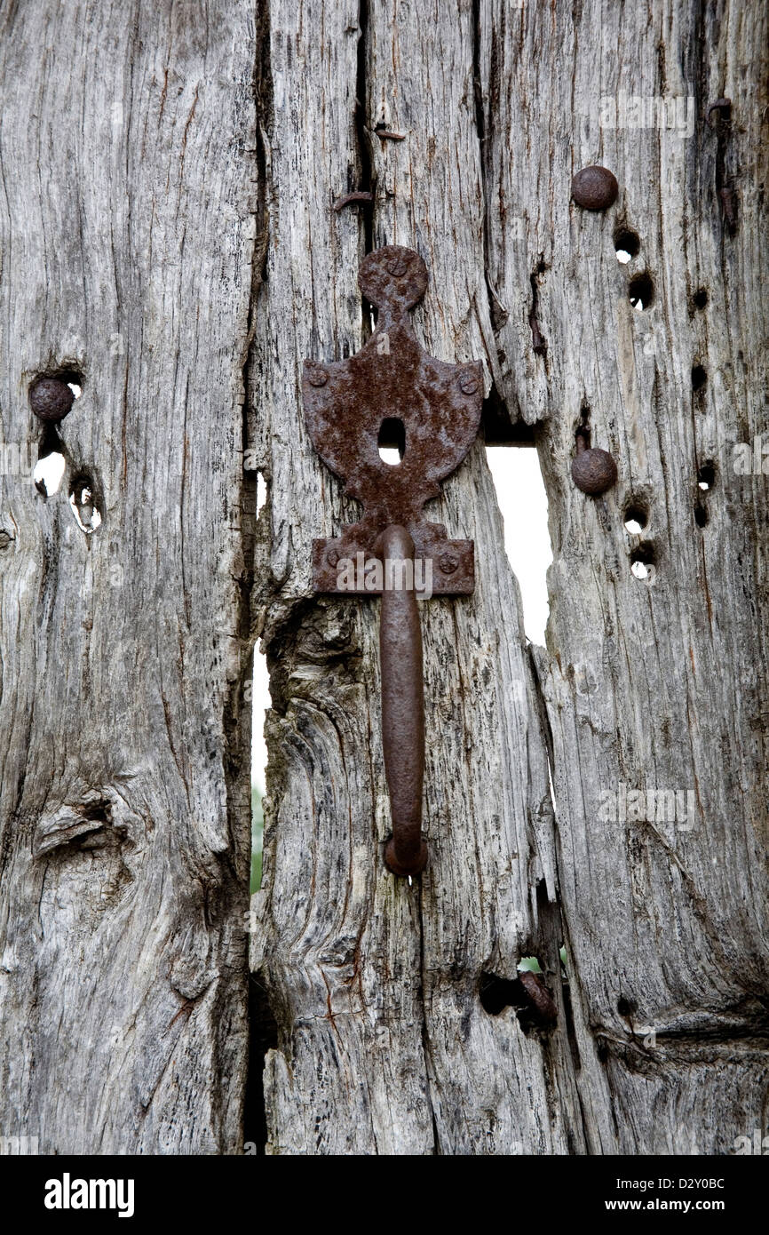 Old wooden door with metal lock and handle, it has bullet hole damage and the wood has turned silvery and cracked. Stock Photo