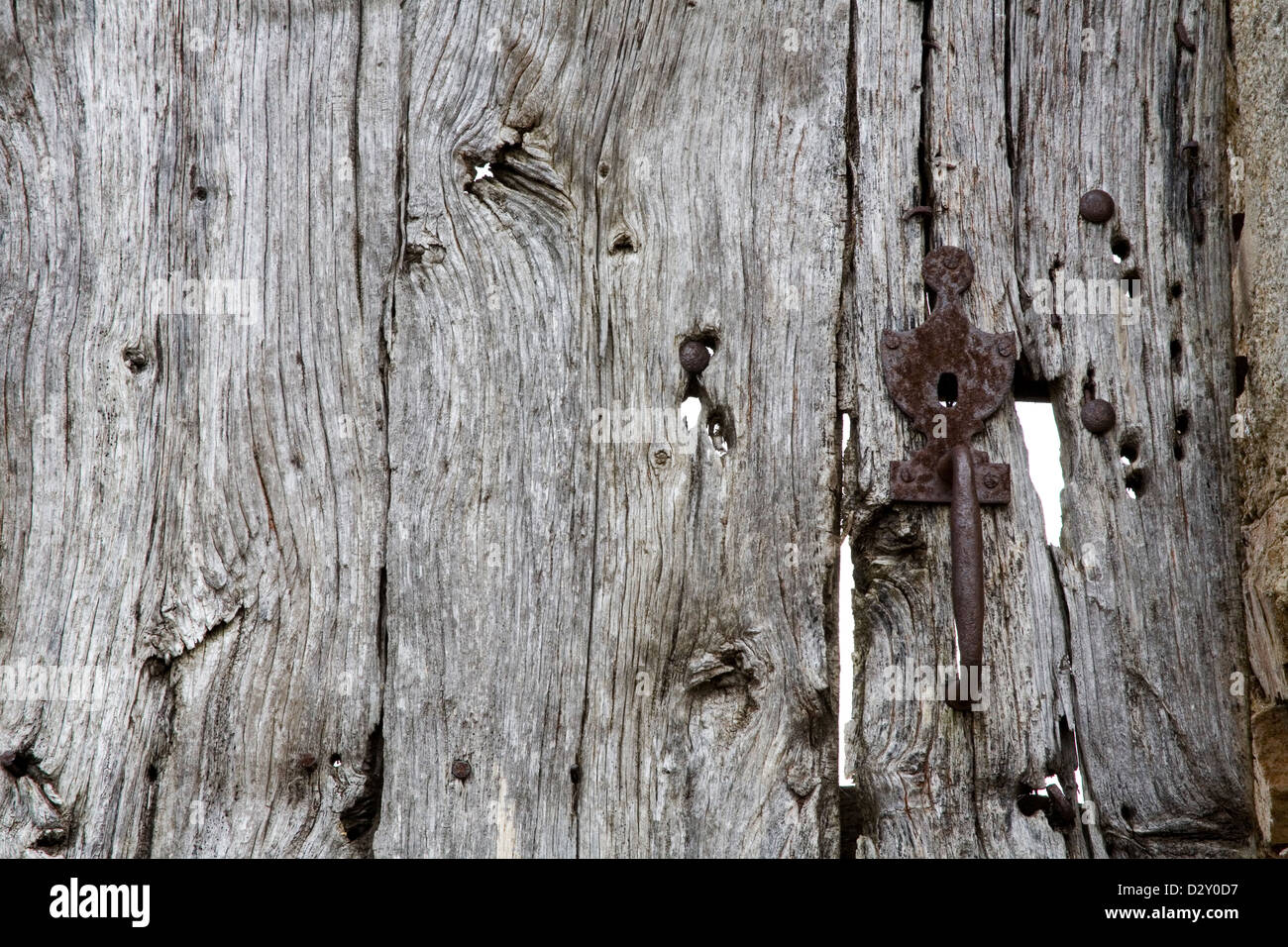 Old wooden door with metal lock and handle, it has bullet hole damage and the wood has turned silvery and cracked. Stock Photo
