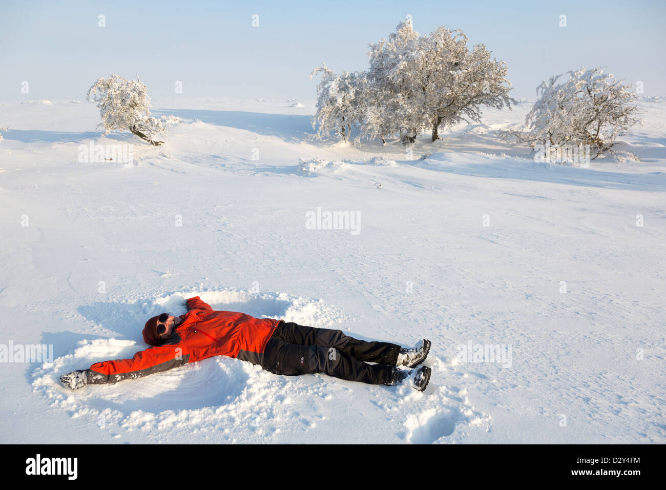 Woman in red coat making a snow angel, Wales, UK Stock Photo