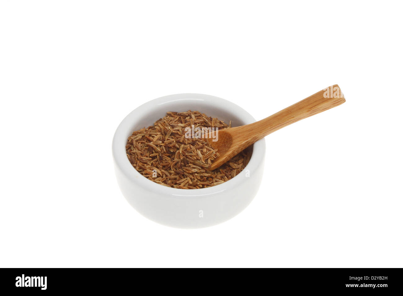 Cumin seeds in a ramekin with a wooden spoon isolated against white Stock Photo