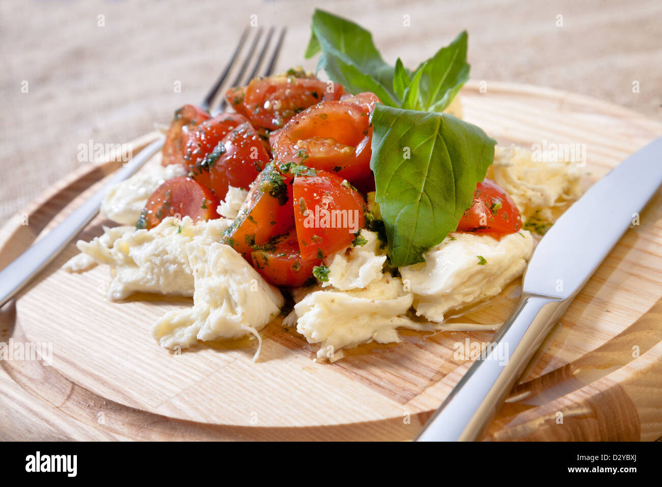 Caprese salad on a round wooden peel with fork and knife Stock Photo ...