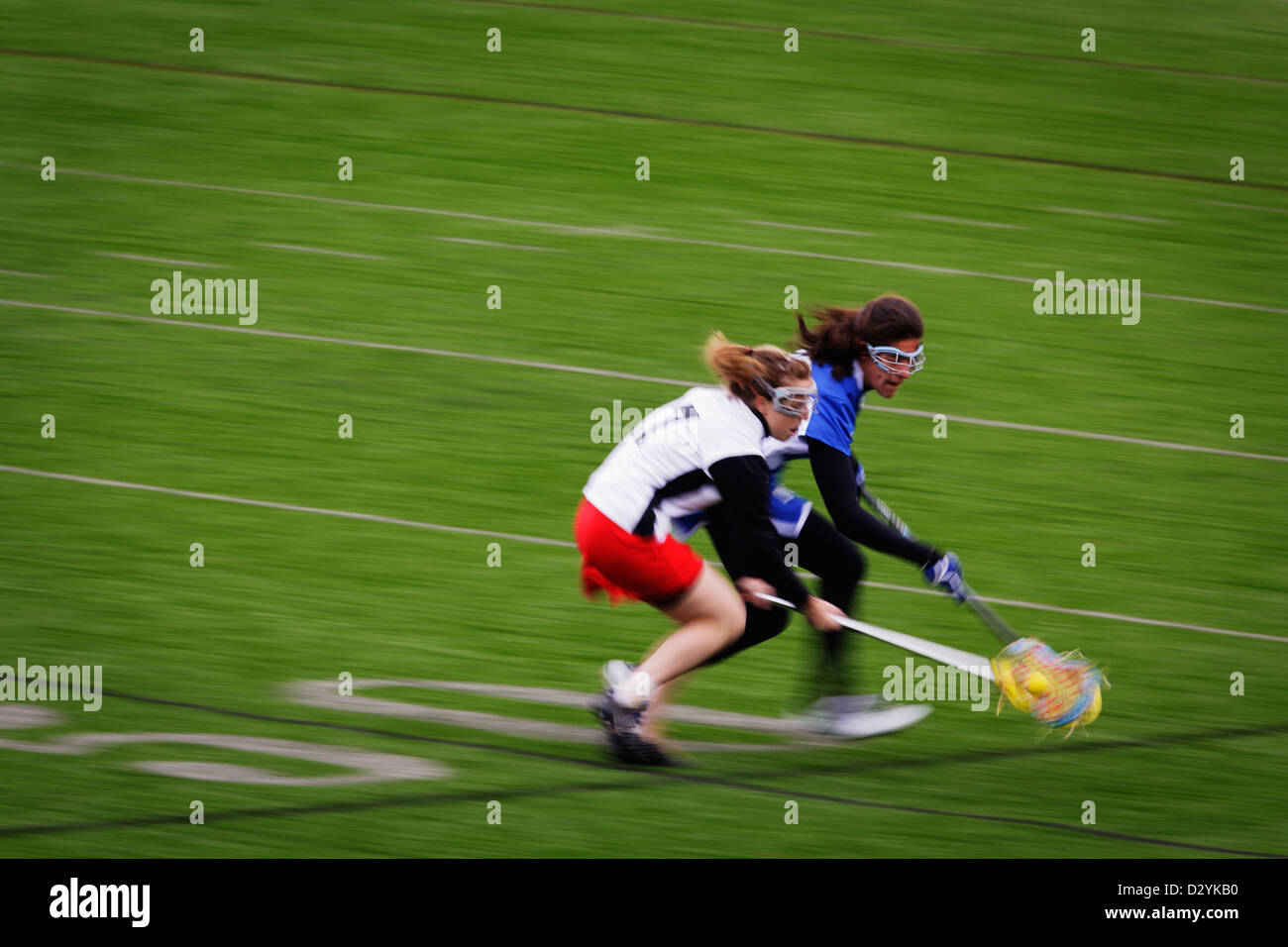 Pan blur of a Catholic University player and Marymount University player reaching for the ball during a lacrosse game. Stock Photo