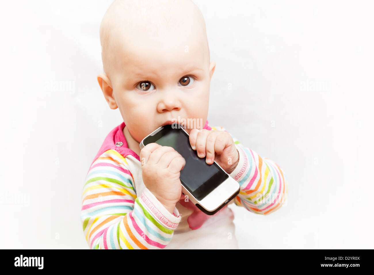 little baby baby chews on a mobile phone in colorful clothing Stock Photo