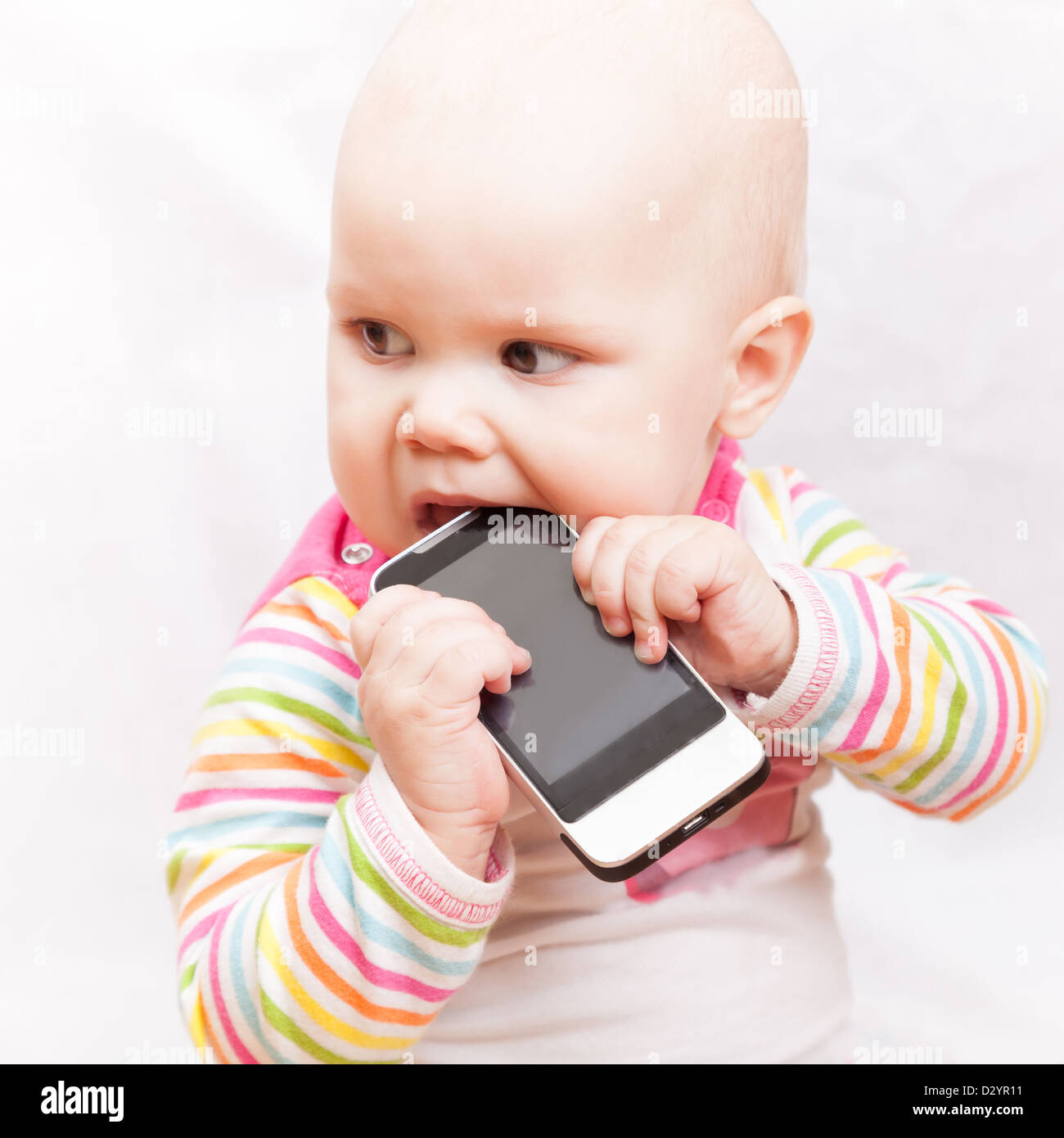 little baby chews on a mobile phone in colorful striped clothing Stock Photo