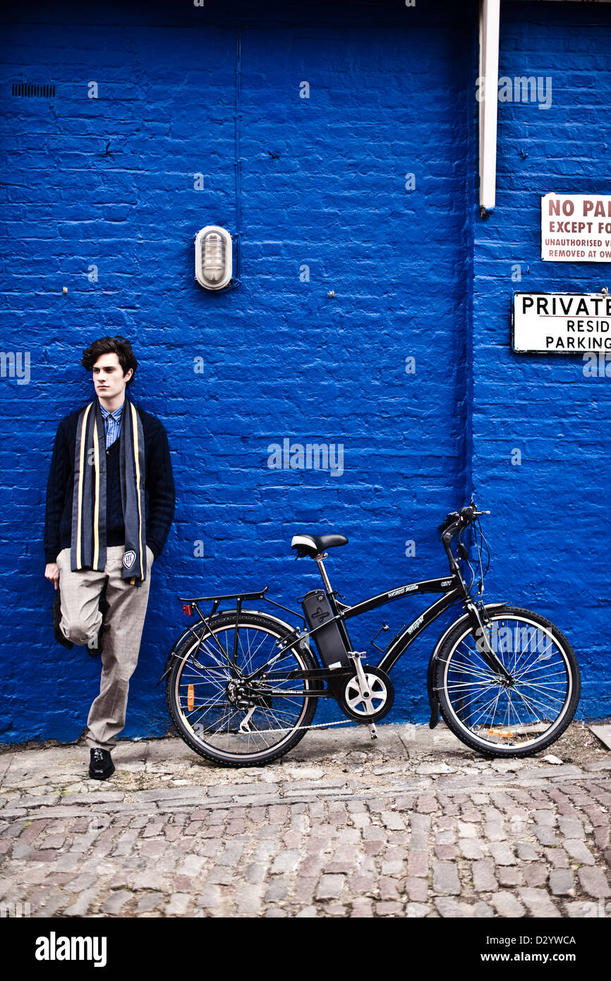 Man stands with electric bike with blue wall, London, UK Stock Photo