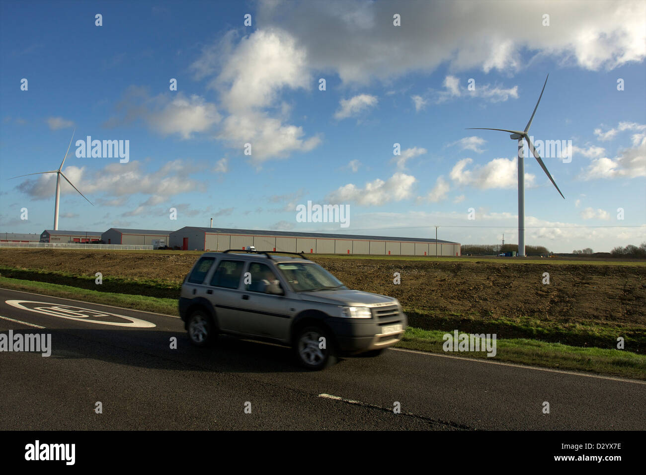 A Car Driving past Eye Industrial Estate's new wind turbines Stock Photo