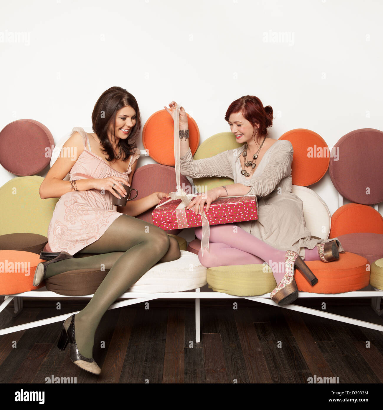 two beautiful girls sitting on a colorful sofa laughing and trying to ...