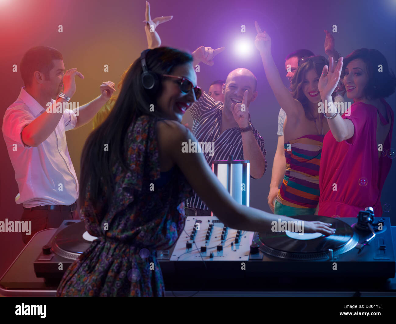 close-up of attractive female dj with headphones spinning records at a party with young happy dancing people and colorful lights Stock Photo