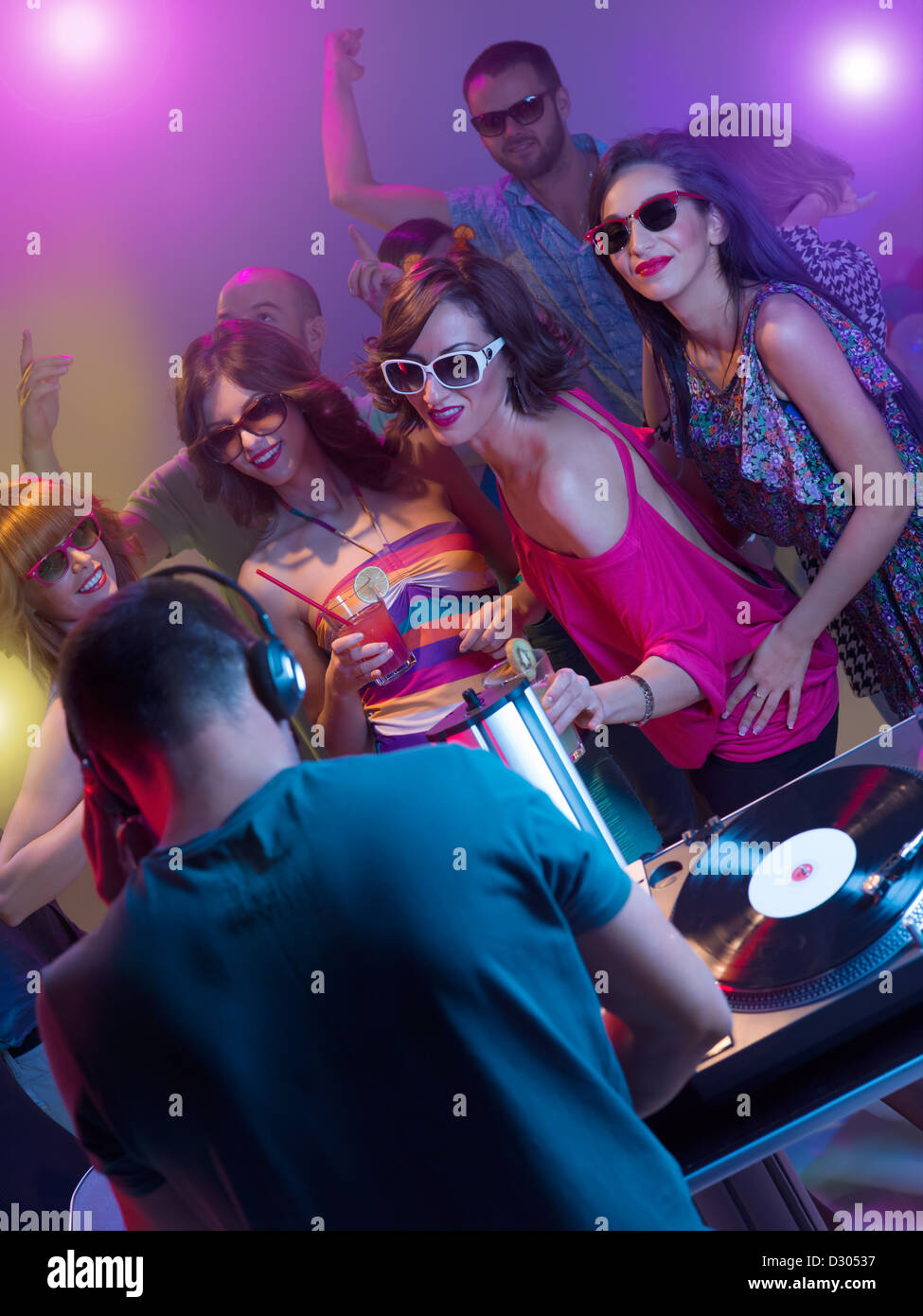 dj mixing music with turntables and headphones in front of young dancing people with sunglasses