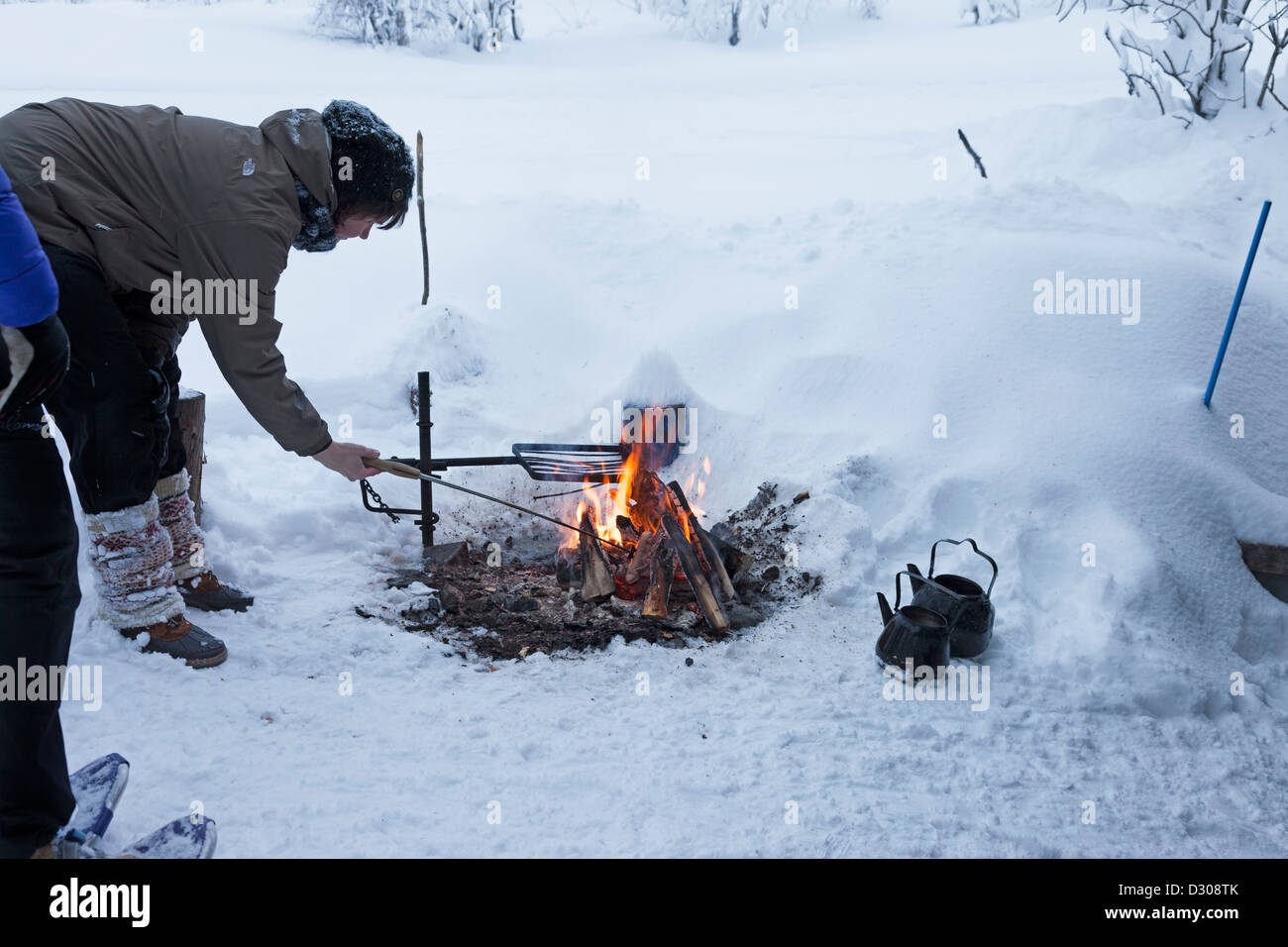 Person Cooking Sausages on an Open Camp Fire Outside of the Kahvikeidas Laavu (Shelter) in Winter Yllas Lapland Finland Stock Photo