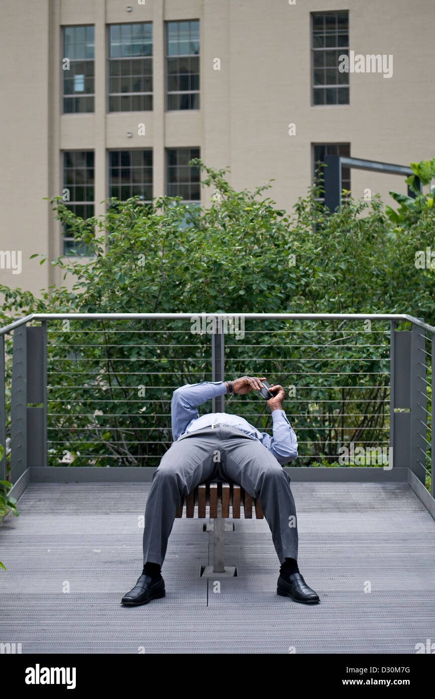 A businessman rests and texts on the High Line, a park in New York City. Stock Photo