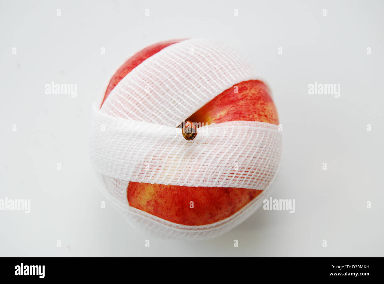A red and yellow apple on a white background, wrapped in a white gauze bandage with an above, or birds eye view of the fruit. Stock Photo