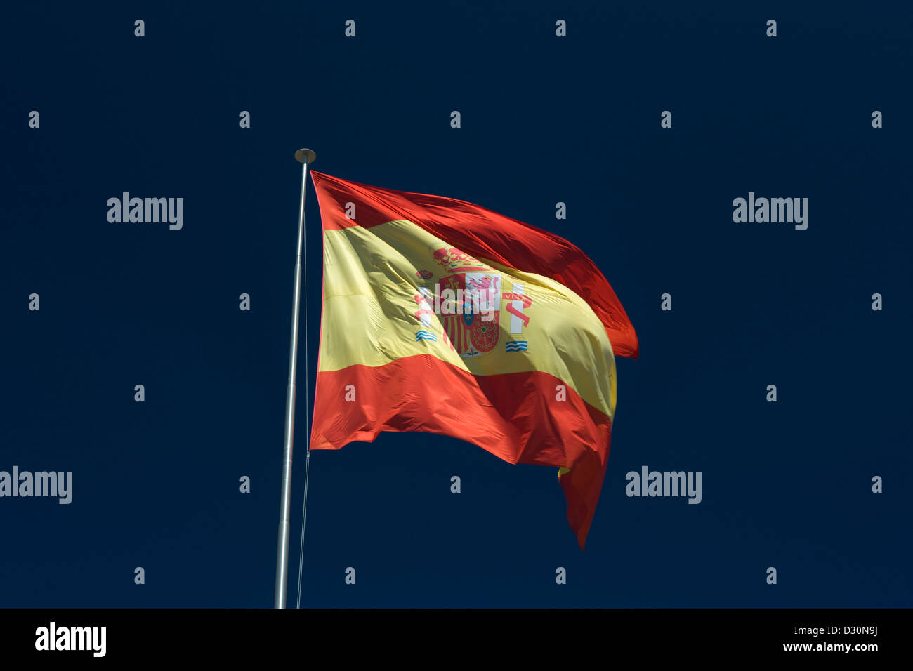 LARGE SPANISH FLAG FLYING ON FLAG POLE WITH BLUE SKY BACKGROUND Stock Photo