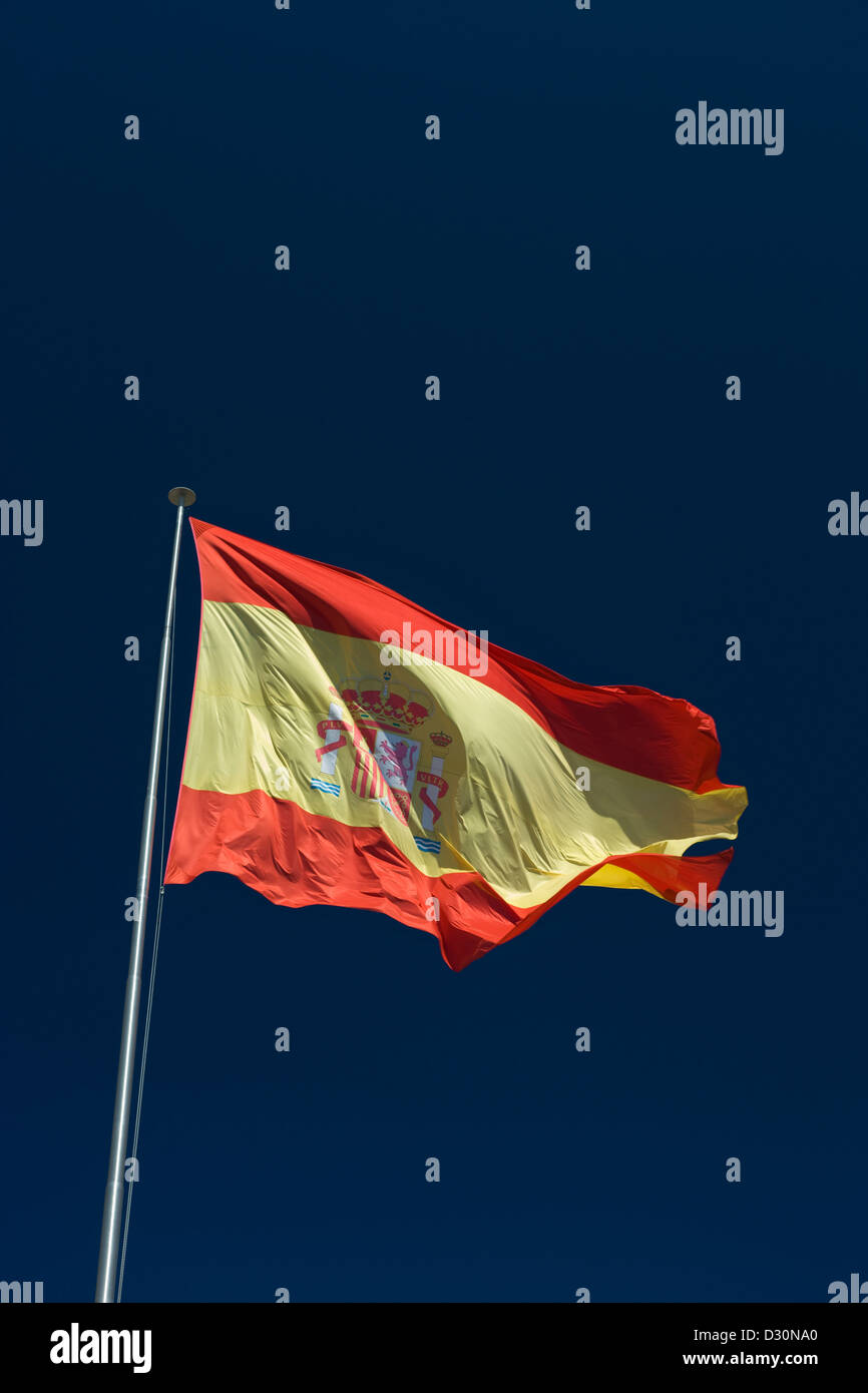 LARGE SPANISH FLAG FLYING ON FLAG POLE WITH BLUE SKY BACKGROUND Stock Photo