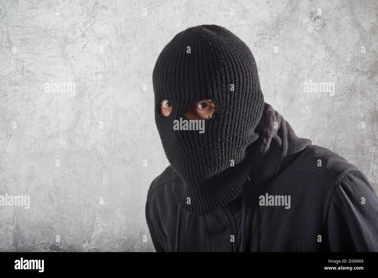 Burglar concept, thief with balaclava caught in front of the grunge concrete wall. Stock Photo